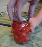 a canned jar of tomatoes and a hand tightening the lid
