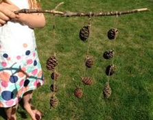 child in white dress holding strings of pinecones on a twig