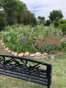 black bench by a garden with purple and red and white flowers encircled by large rocks as a border