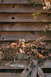 dried leaves and flowers in a pile on a wooden compost bin in front of a wooden fence