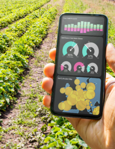 hand is holding cell phone showing various charts and graphs. person holding phone is in a field with green rows of a planted crop 