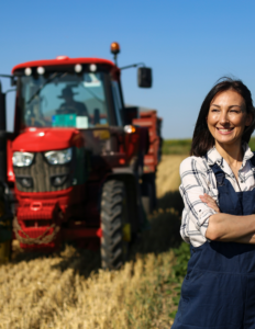 woman wearing blue overalls standing in a field in front of a red tractor with blue sky