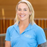 white woman with long shoulder-length blonde hair and blue eyes. she is wearing a light blue polo shirt with "Denver botanic gardens" embroidered in white.